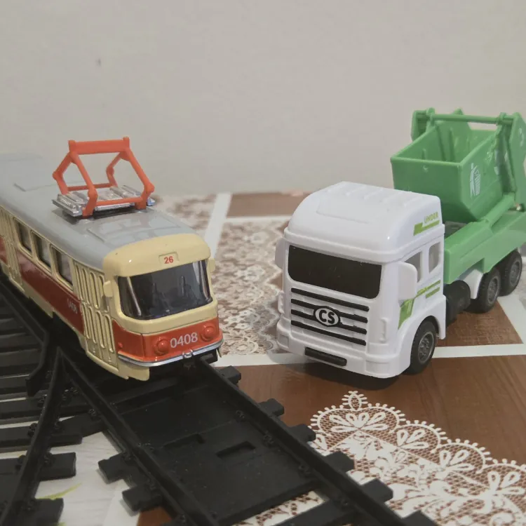 Plastová tramvaj na kolejích a vedle stojící zelené plastové autíčko